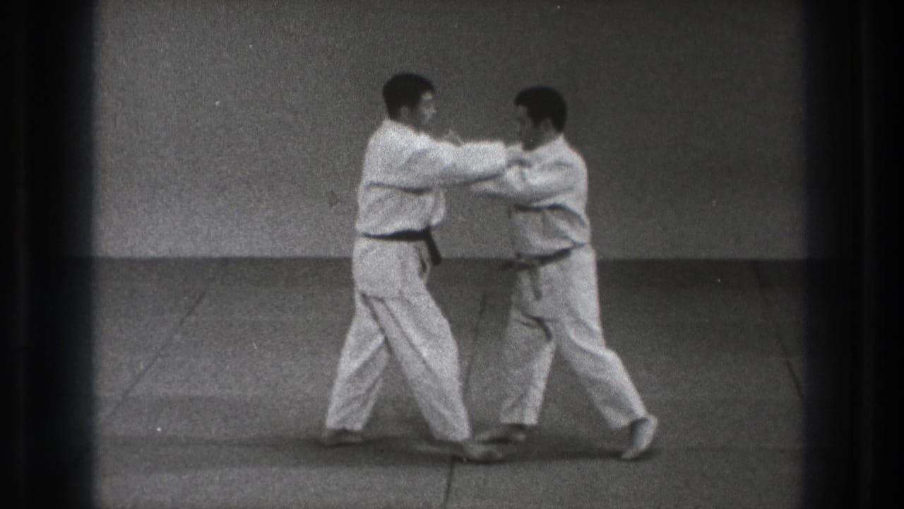 Two men in white karate gi face each other on a mat with hands raised in contact.