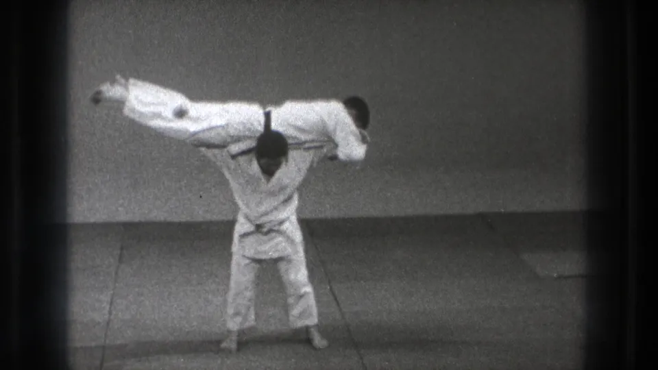 In the Tokyo 1971 martial arts footage, one man raises his partner across his shoulders on the mat during the central throwing motion.