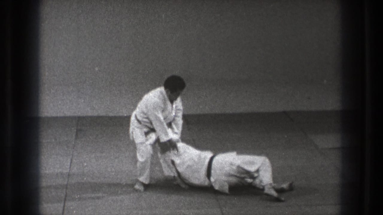Two judo practitioners on a mat, one standing over another lying on his back.