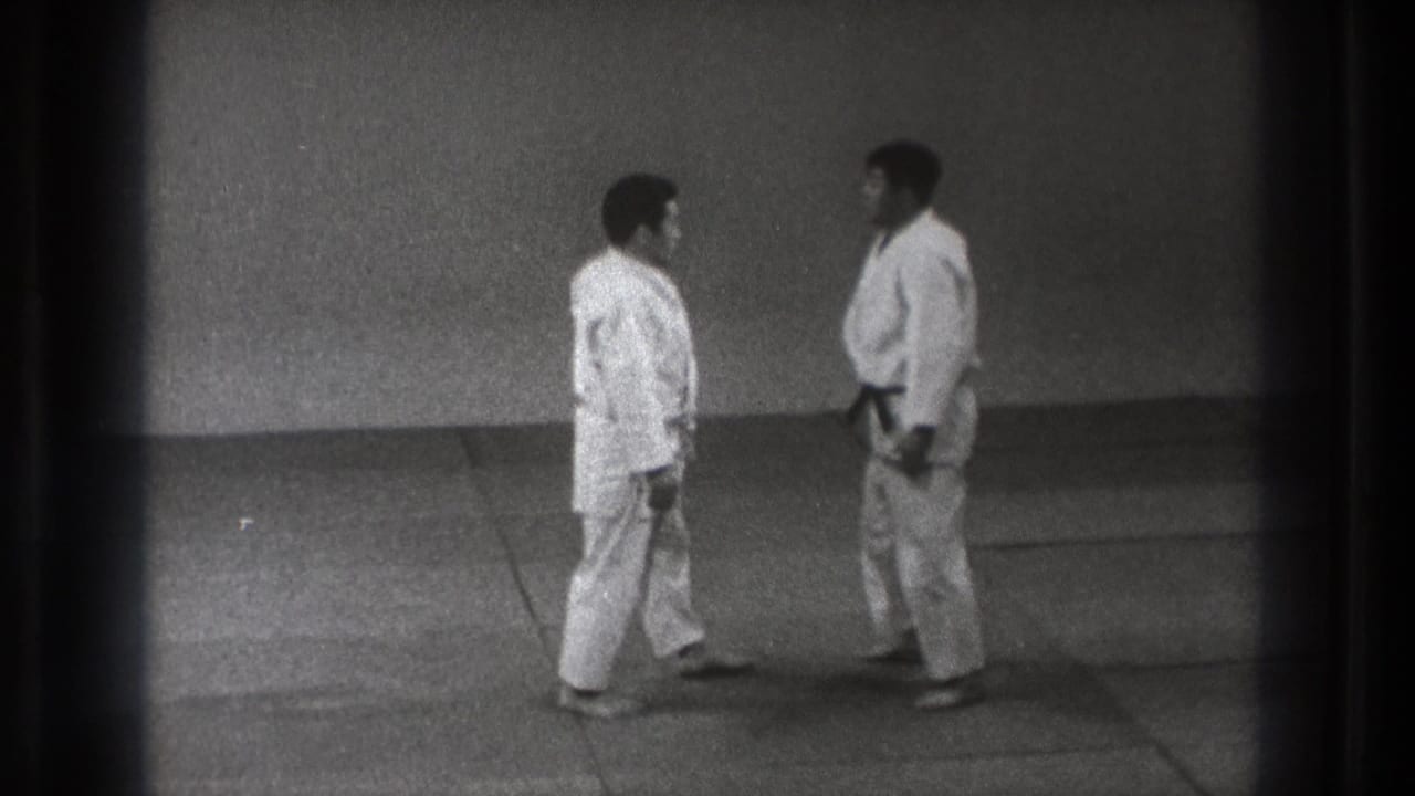 Two men in white gi face each other on a dojo mat.