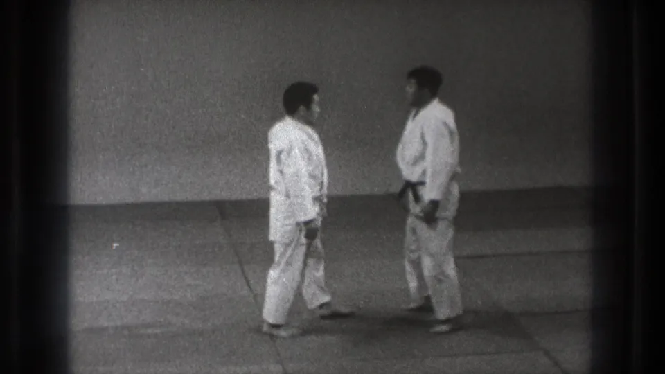 1971 Tokyo frame of two martial arts practitioners facing each other in a dojo, one wearing a dark belt.