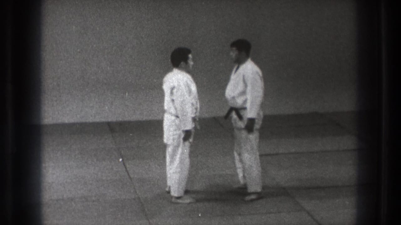 1971 Tokyo home-movie frame showing two men in gi bowing or leaning toward each other during dojo practice.