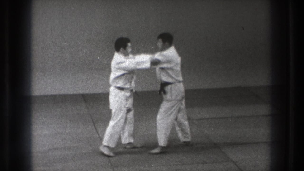 1971 Tokyo frame showing two martial arts practitioners making hand contact during a grip or pushing drill on the mat.