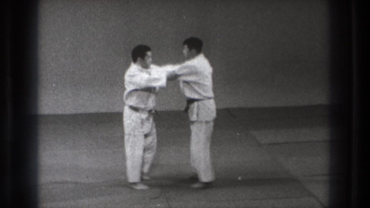 In 1971 Tokyo footage, two karate students in white gi stand facing each other during partner practice on a matted floor.