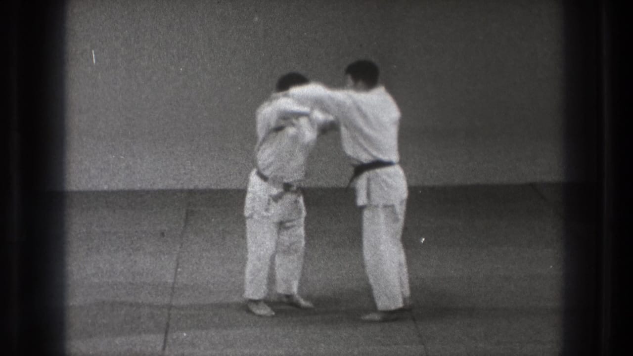 Two karate students in white gi practice a close mutual hold in a sparse Tokyo training room, filmed on 8mm in 1971.