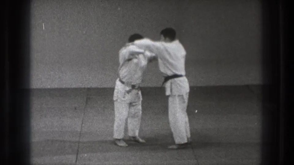 Two karate students in white gi practice a close mutual hold in a sparse Tokyo training room, filmed on 8mm in 1971.