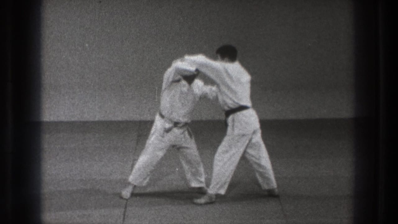 A karate student bends under a partner's arm during a controlled break or restraint drill in 1971 Tokyo home-movie footage.