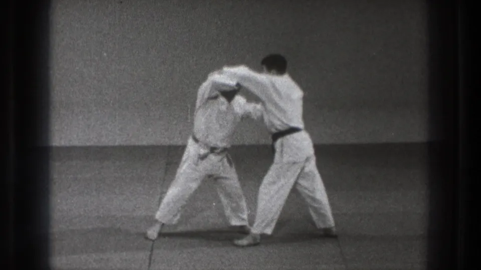 A karate student bends under a partner's arm during a controlled break or restraint drill in 1971 Tokyo home-movie footage.
