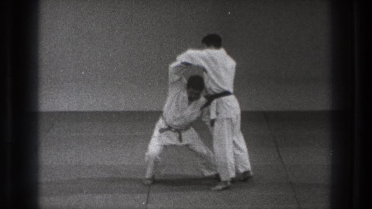 Two martial artists in white gi begin a close grappling exchange on a mat.