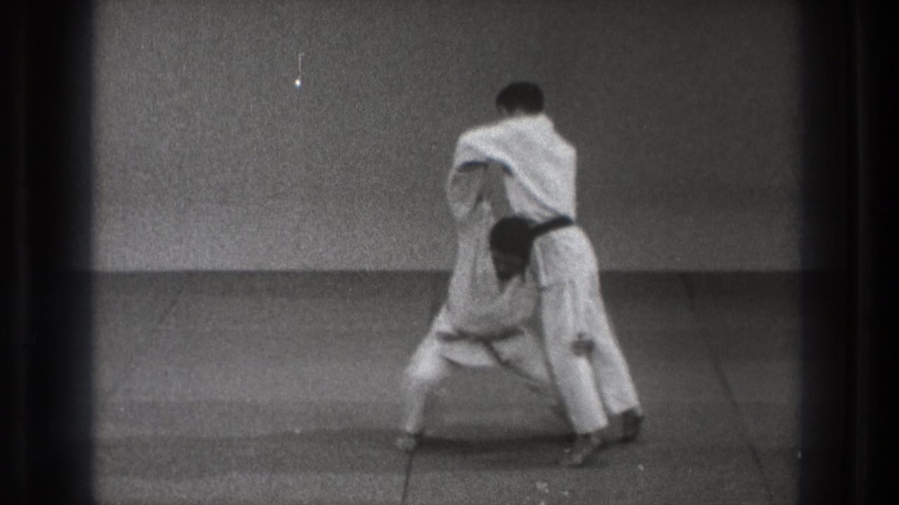 In 1971 Tokyo karate footage, one black-belt practitioner braces while controlling his partner during a throw setup.