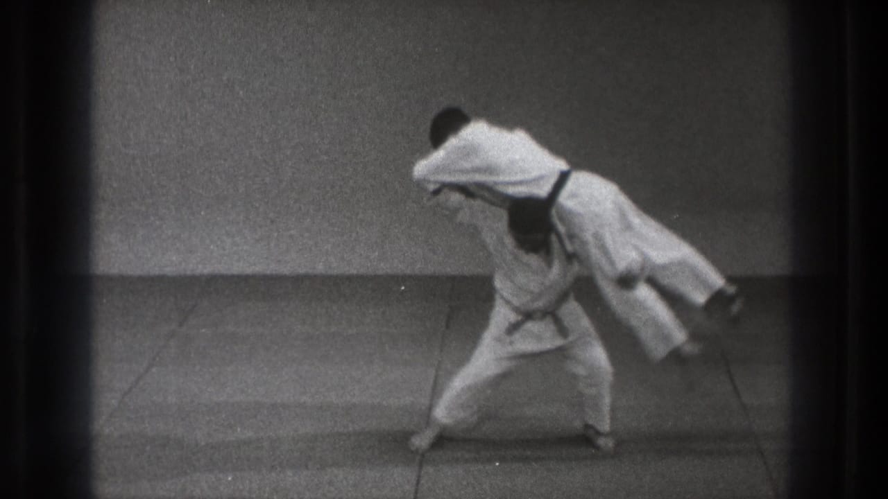 The throw reaches its peak as one martial artist lifts his partner nearly horizontal on a plain mat in 1971 Tokyo footage.