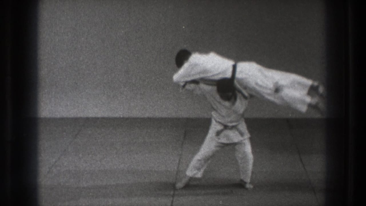 In 1971 Tokyo footage, one martial artist in a white gi lifts another across his shoulders during a demonstration.