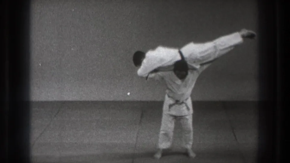 The Tokyo martial arts demonstration shows one gi-clad practitioner holding his partner nearly horizontal in a lift.