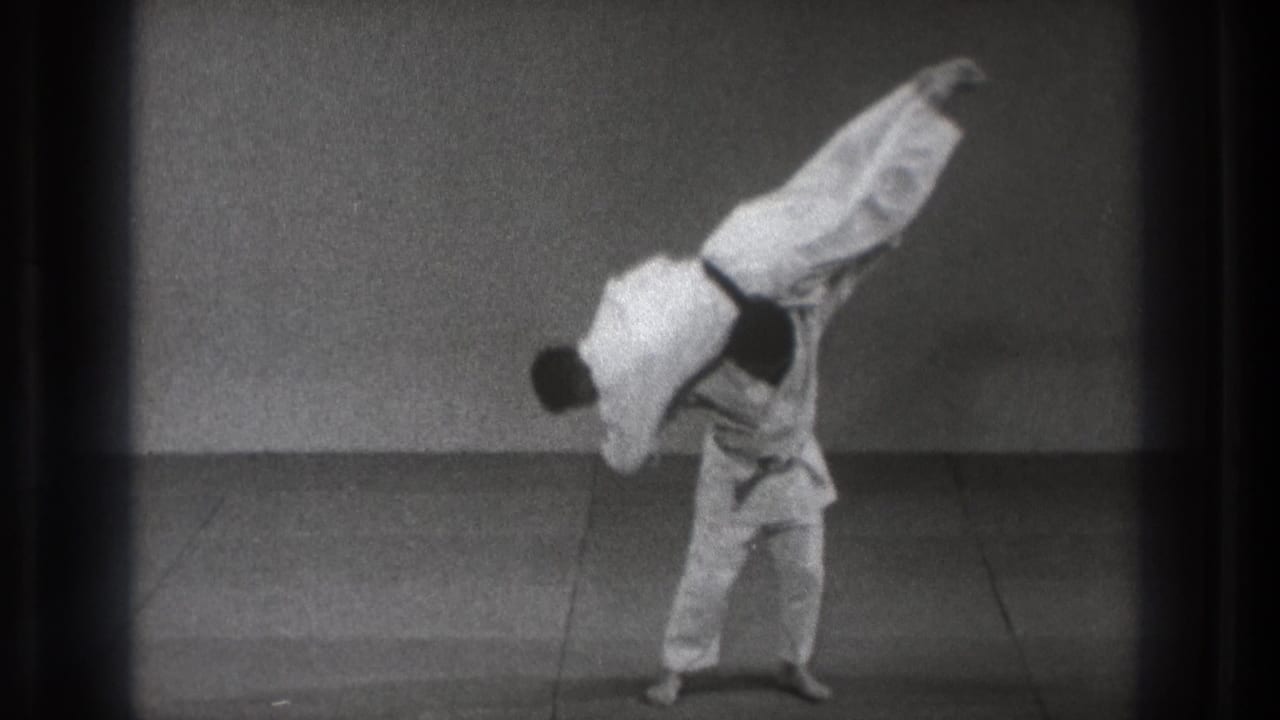 The demonstration reaches a high carry position, with one practitioner elevated over the other's shoulder line.