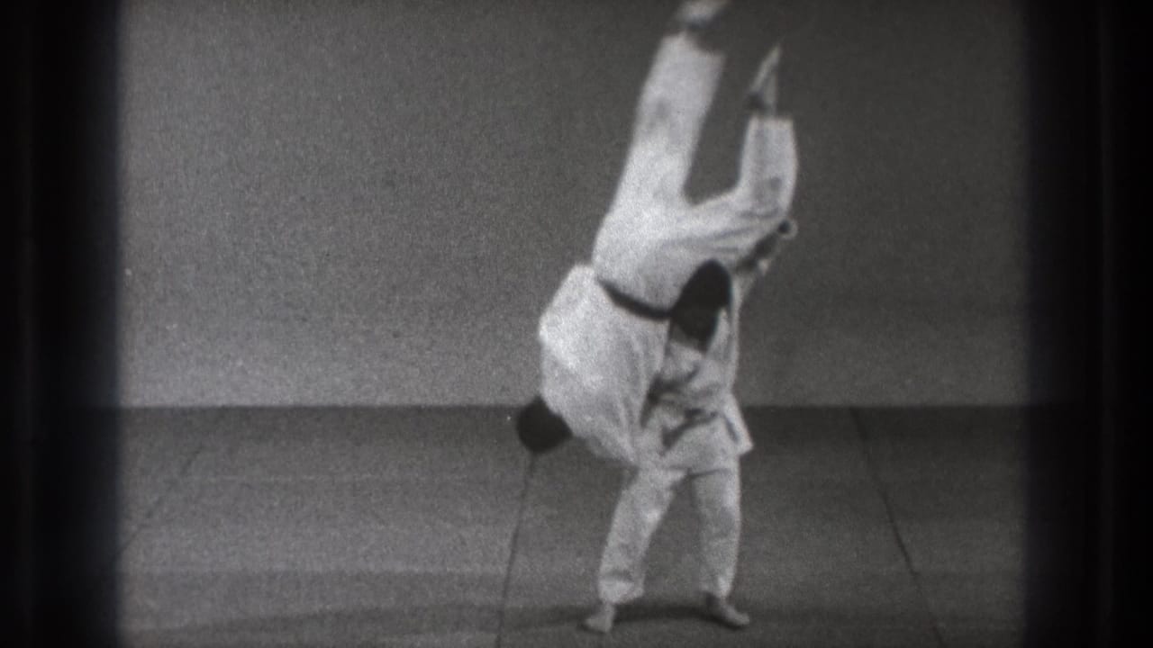 Two men in white judo uniforms begin a throw on a mat.