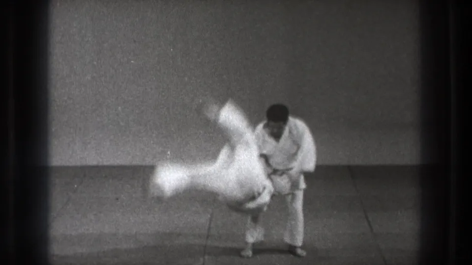 In the 1971 Tokyo home-movie frame, a judo practitioner completes a fast throw as the other man rotates through the air.
