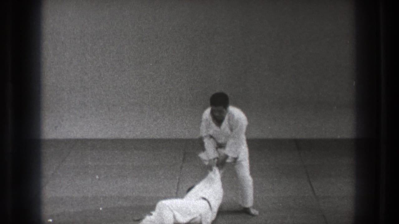 The Tokyo judo practice continues as one man stands over his partner, who is down on the mat after the throw.