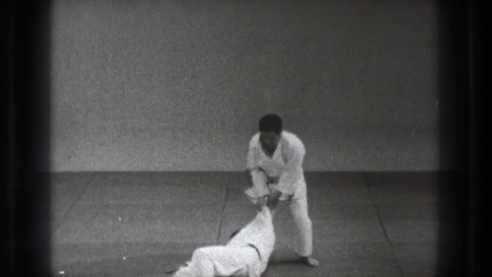 The Tokyo judo practice continues as one man stands over his partner, who is down on the mat after the throw.