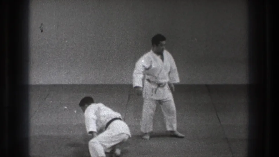 1971 Tokyo 8mm frame showing two barefoot men in white martial arts uniforms preparing on a plain mat.