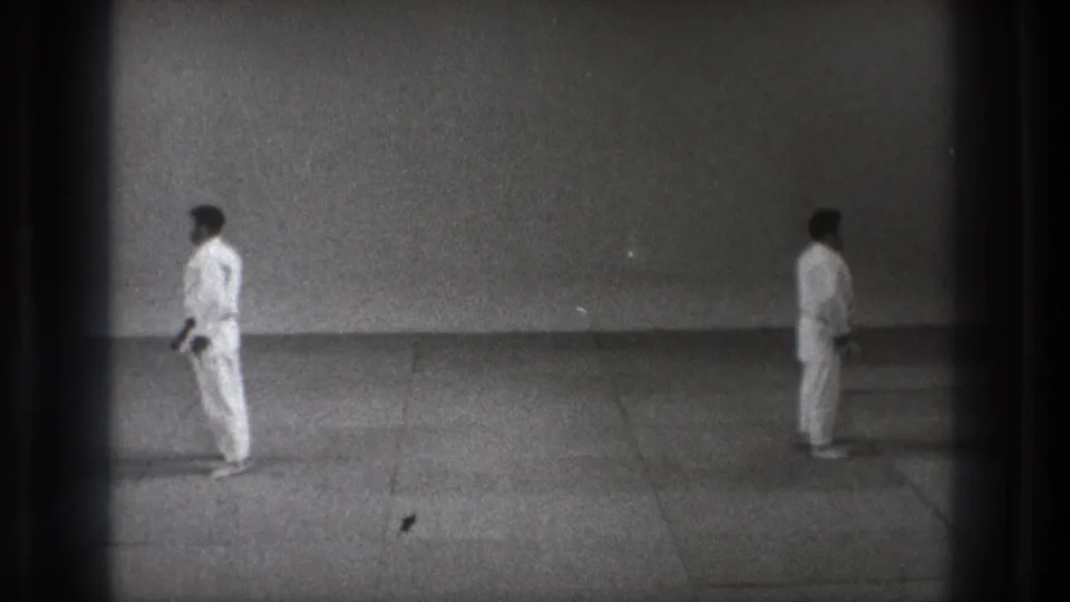 1971 Tokyo 8mm frame showing two martial artists in white gi standing apart in a sparse training space.