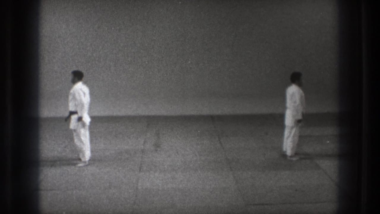 1971 Tokyo 8mm frame with two martial artists in white gi holding spaced stances in a plain dojo-like room.