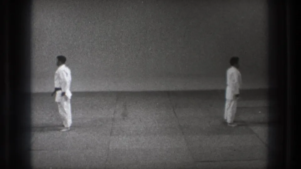 1971 Tokyo 8mm frame with two martial artists in white gi holding spaced stances in a plain dojo-like room.