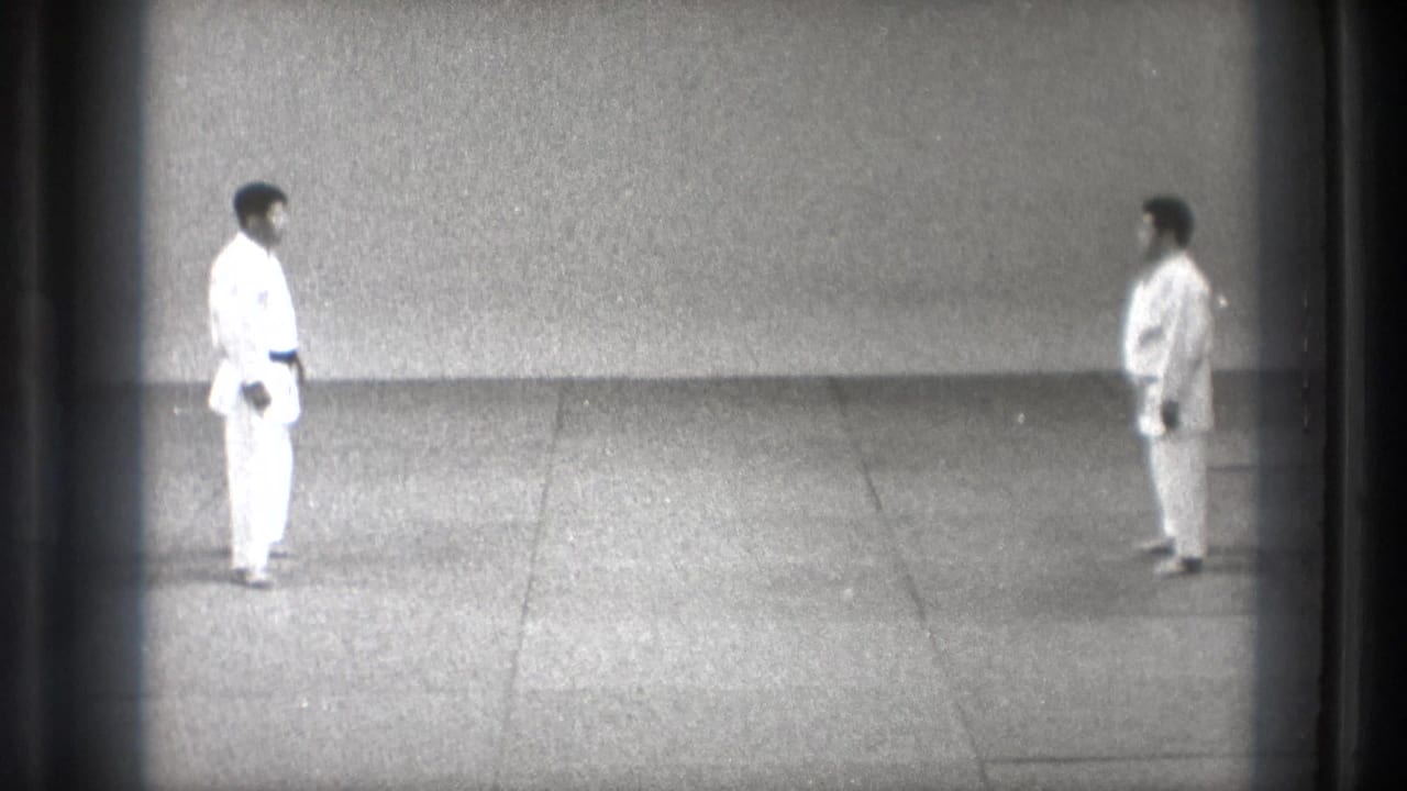 Two adult martial-arts practitioners in white gi face each other in a sparse Tokyo dojo setting, based on supplied 1971 metadata.