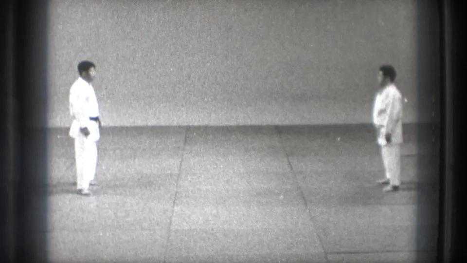Two adult martial-arts practitioners in white gi face each other in a sparse Tokyo dojo setting, based on supplied 1971 metadata.