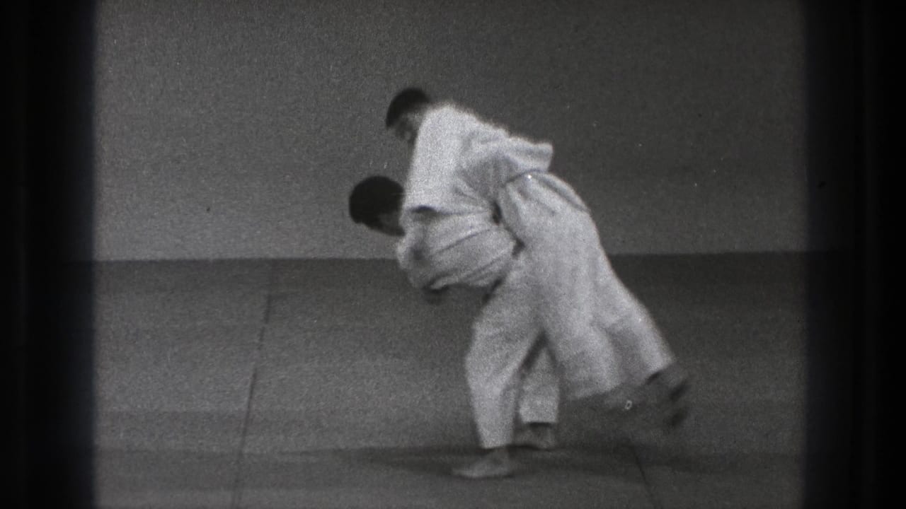 The martial artists are locked in a close throw or takedown movement on the dojo mat in this black-and-white 8mm frame.