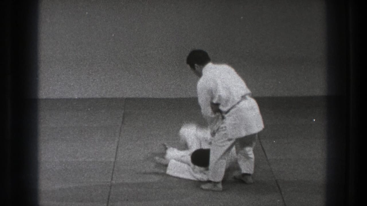 Two judo practitioners in white gi during a throw on a padded mat.