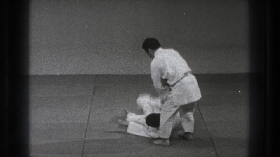 In 1971 Tokyo footage, one judo practitioner in a white gi throws another on a padded indoor mat.