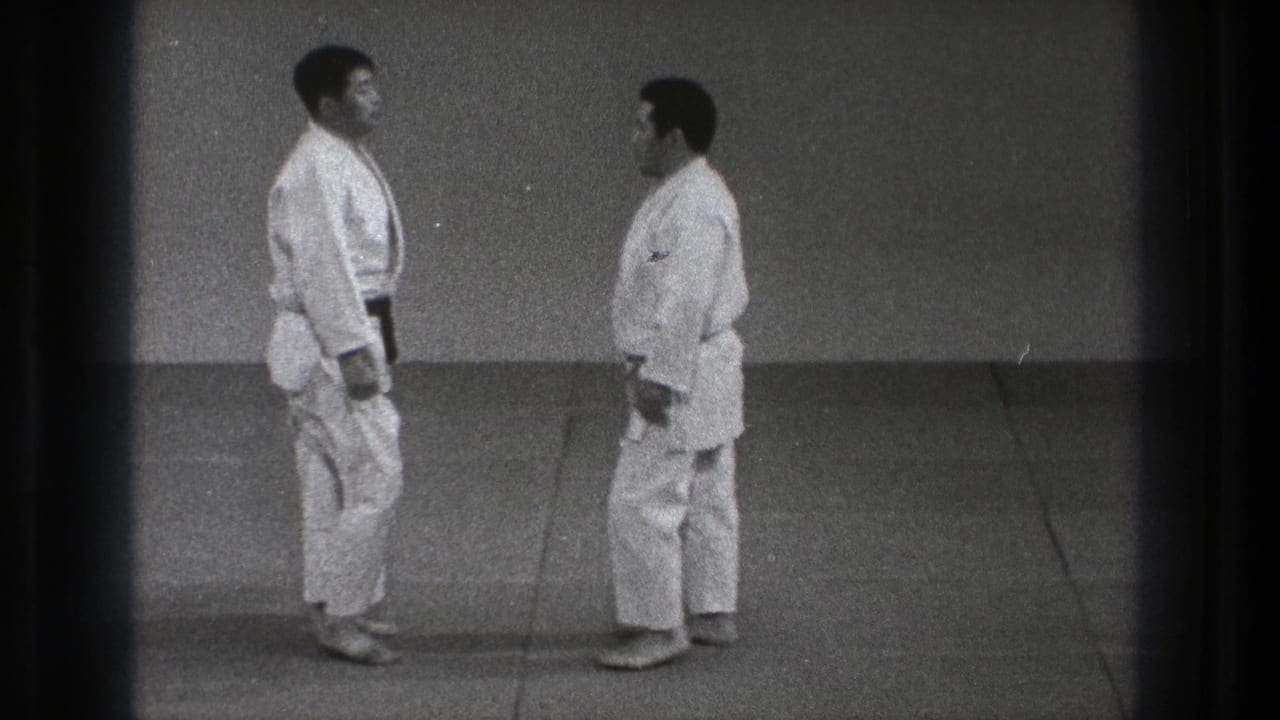 Two judoka in white gi stand on a mat facing each other.