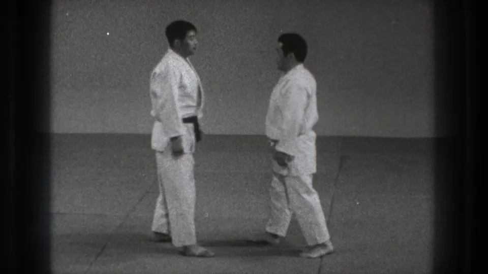 Two judoka in white gi approach each other on a dojo mat in archival 1971 Tokyo footage.