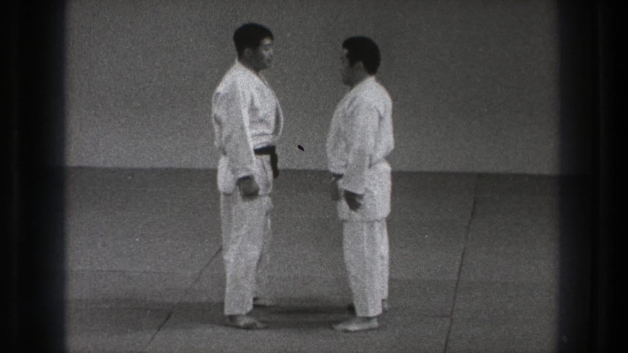 Two adult judoka stand face to face on a dojo mat, preparing for contact in Tokyo, 1971 footage.