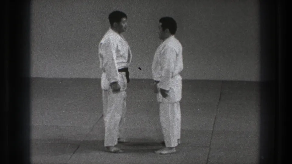 Two adult judoka stand face to face on a dojo mat, preparing for contact in Tokyo, 1971 footage.