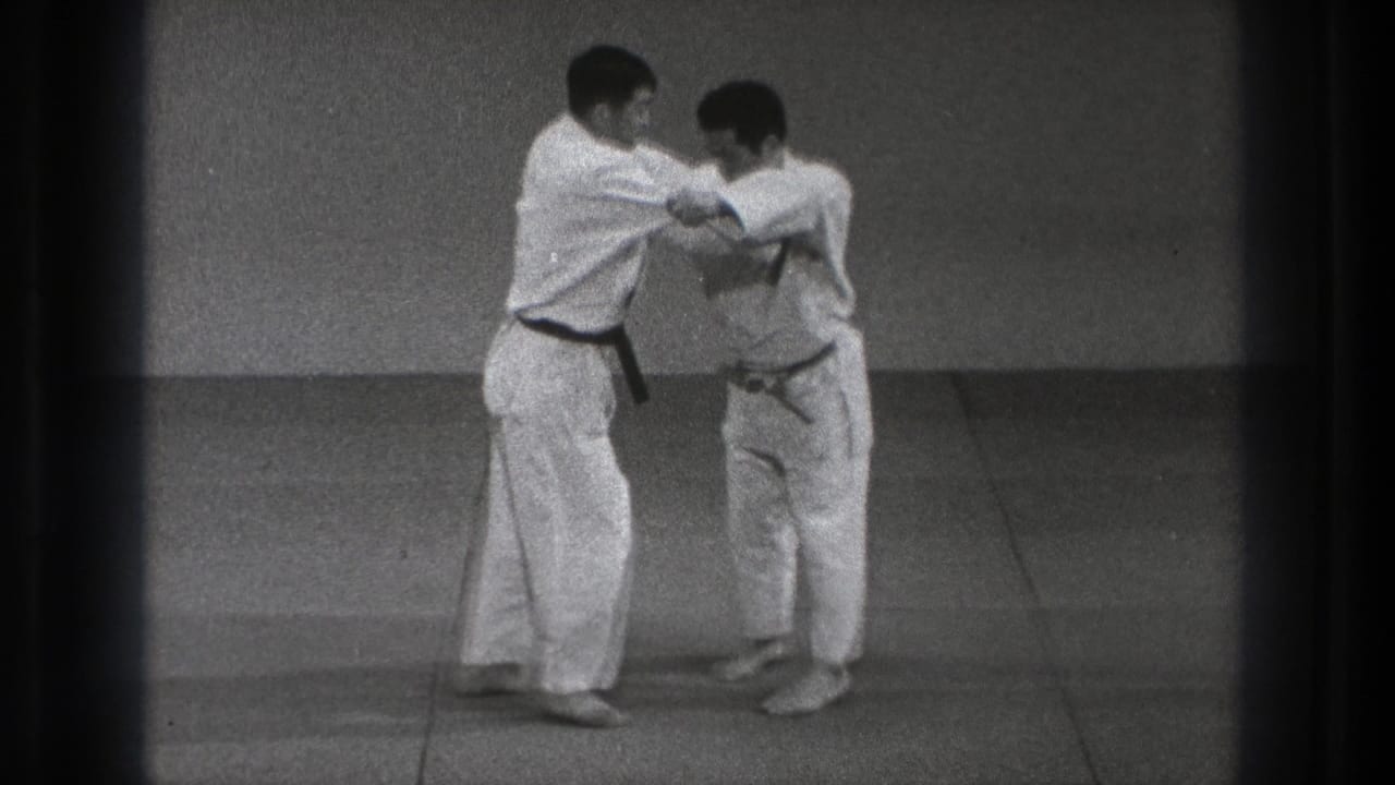 The black-belt practitioner shifts his partner's balance during a martial arts throwing sequence in the Tokyo dojo setting.