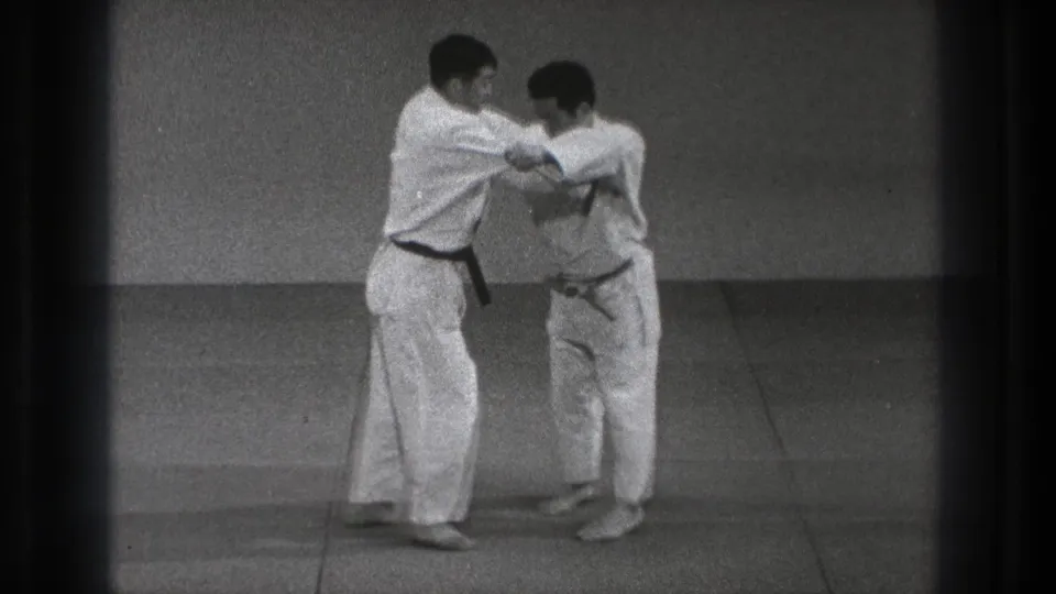 The black-belt practitioner shifts his partner's balance during a martial arts throwing sequence in the Tokyo dojo setting.