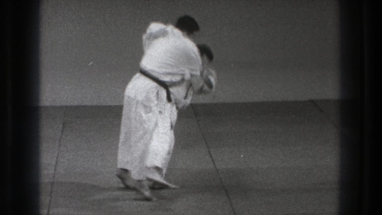 The black-belt practitioner enters the throw, pulling his partner forward across the mat in the 1971 Tokyo training footage.