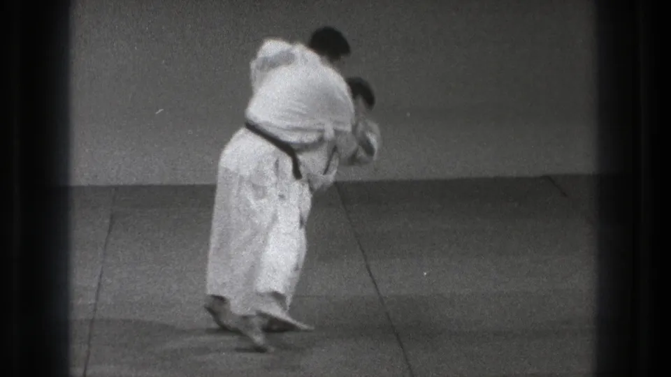 The black-belt practitioner enters the throw, pulling his partner forward across the mat in the 1971 Tokyo training footage.