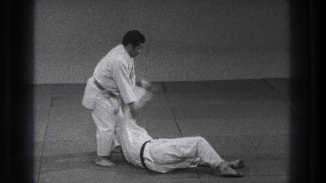 Two men in white gi on mats as one stands over the other on the floor.