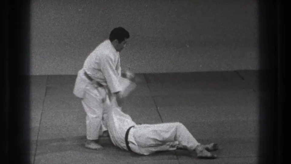 In 1971 Tokyo footage, one man in a white gi holds or releases another man lying on a mat during martial arts practice.