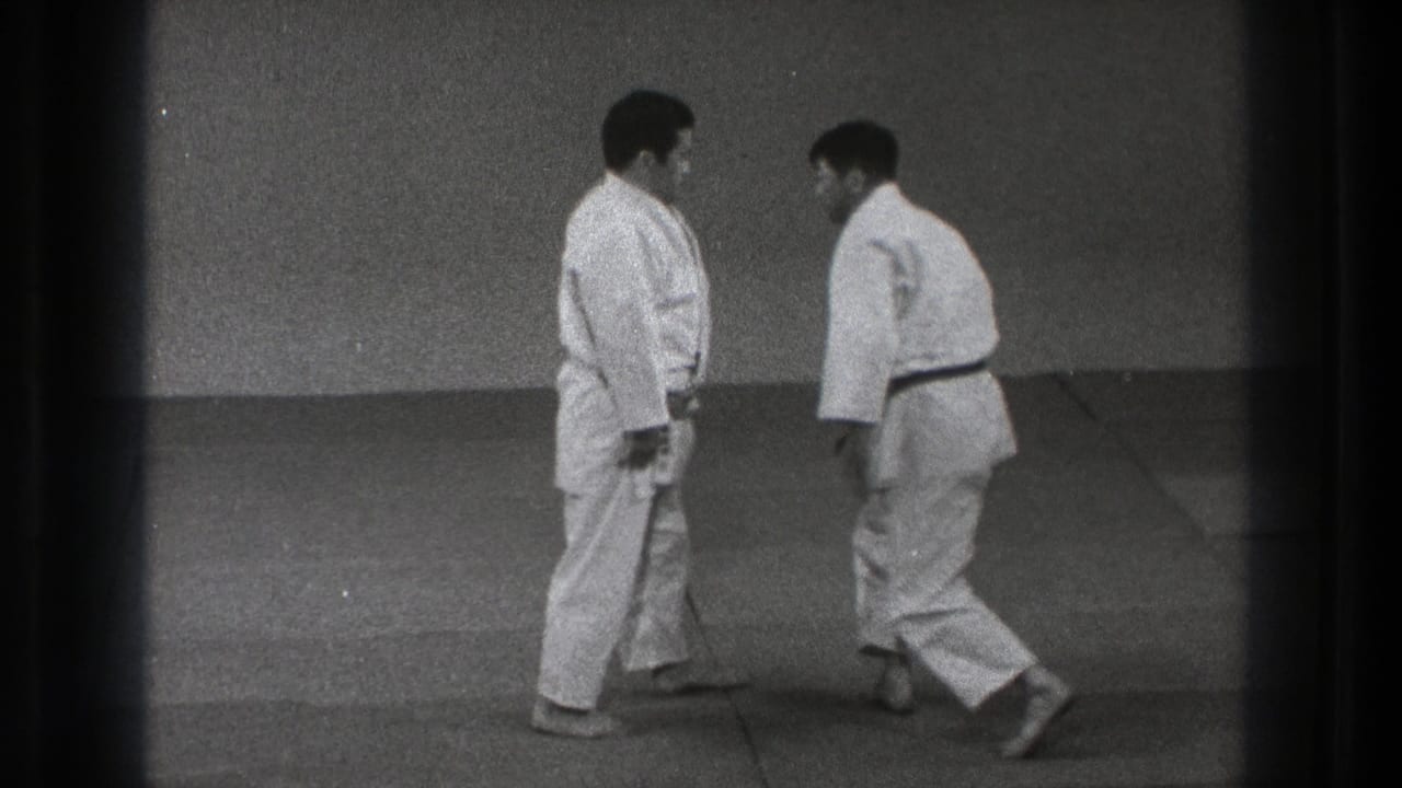 Two adult men in white gi and dark belts face each other on mats during a brief karate or martial arts training reset in Tokyo.