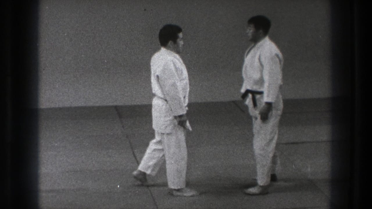 Two martial arts practitioners stand face to face on mats in a quiet training room, shown in 1971 Tokyo 8mm footage.