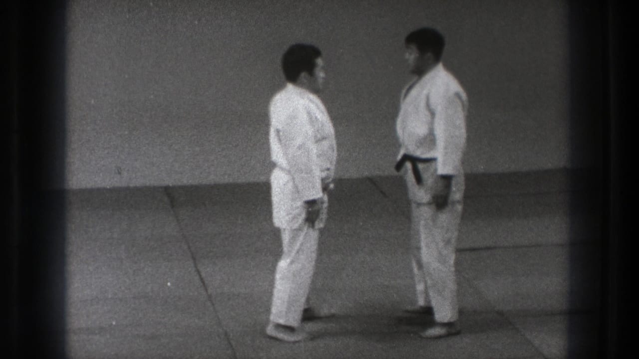 Two adult men in white gi stand facing each other on a mat.