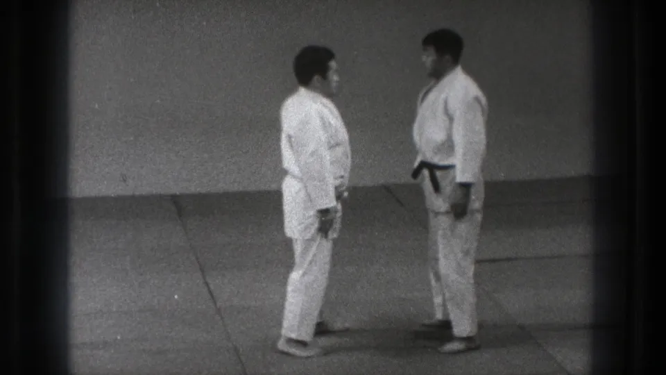 In 1971 Tokyo footage, two adult men in white martial arts uniforms stand face to face on an indoor mat before beginning practice.