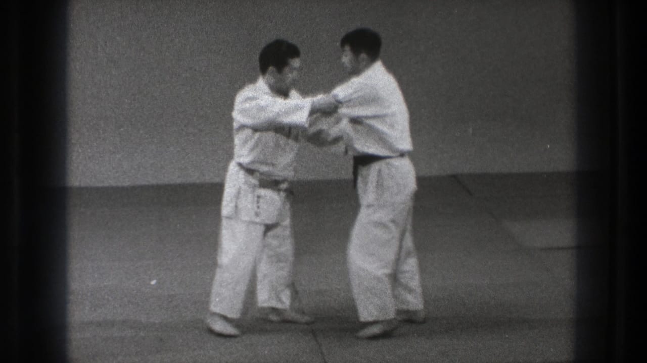 The drill continues as both men maintain sleeve and arm contact while standing on the mat in the indoor practice space.