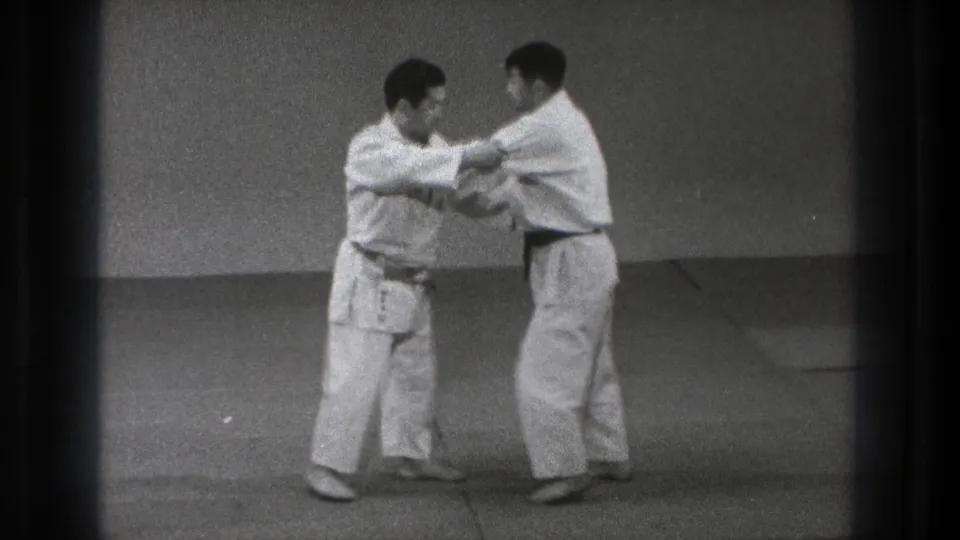 The drill continues as both men maintain sleeve and arm contact while standing on the mat in the indoor practice space.
