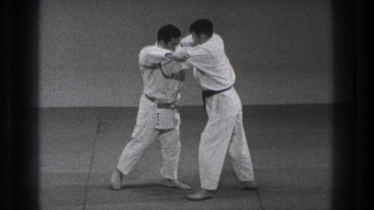 One adult practitioner steps in and turns his body while maintaining a grip, suggesting a defensive control technique in the dojo practice sequence.