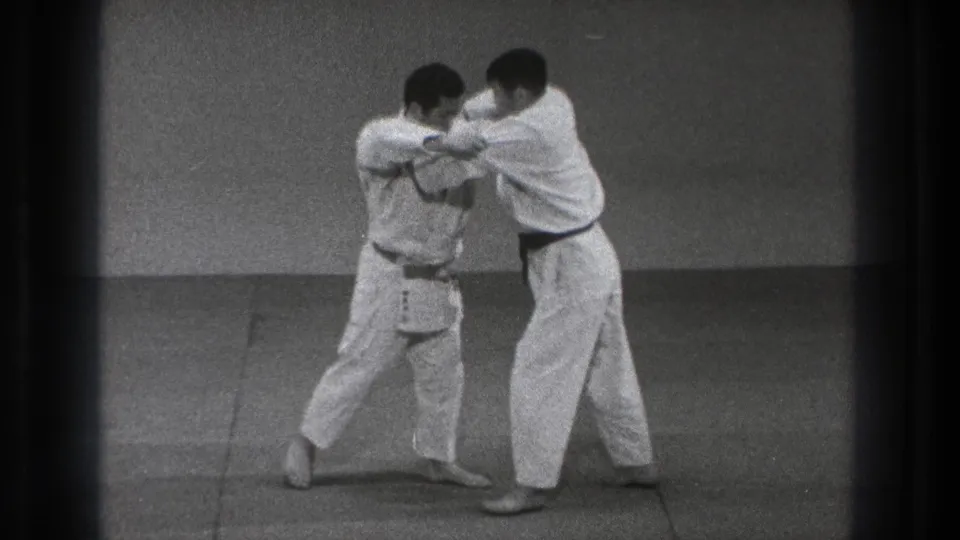 One adult practitioner steps in and turns his body while maintaining a grip, suggesting a defensive control technique in the dojo practice sequence.