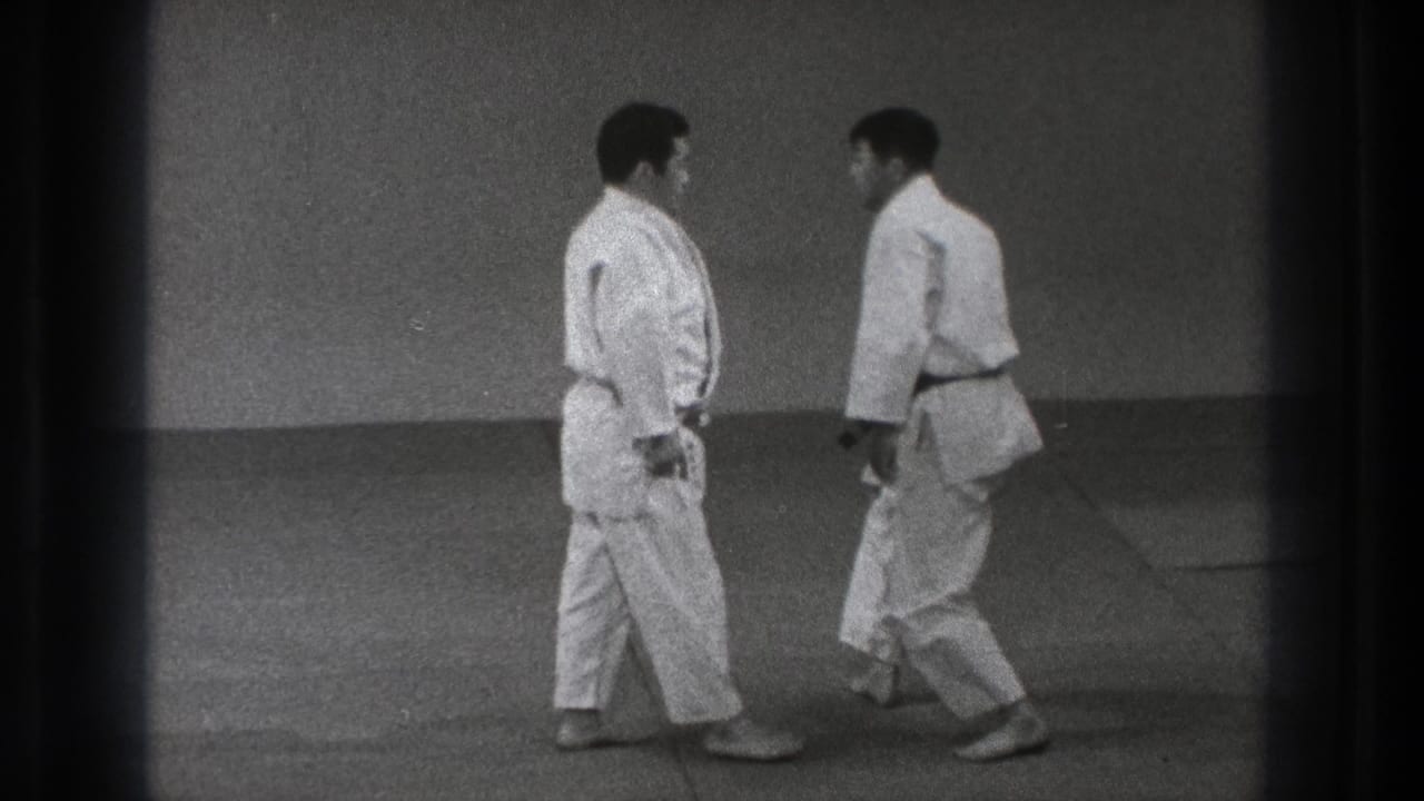 Two men in white karate uniforms face each other on mat flooring.
